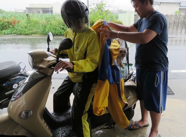 兩人冒雨騎機車合力載兩隻貴賓狗到狂犬病疫苗注射站。蕭士塔/攝