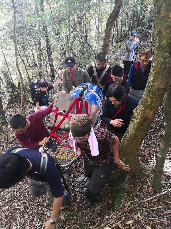 由山林到車道需上爬百餘公尺,森林護管員輪流將負有黑熊運輸桶的擔架扛上山。東勢處提供。