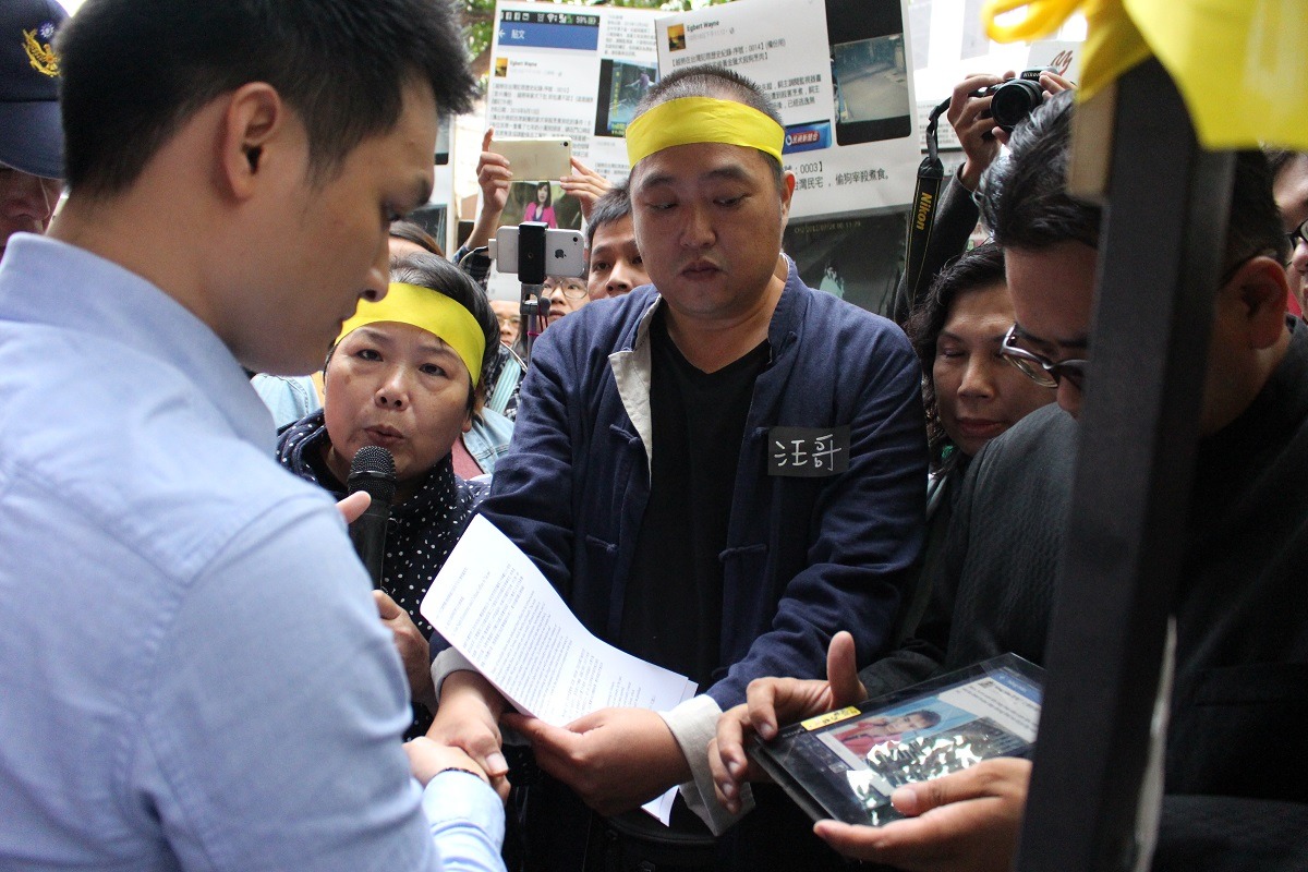 駐台北越南經濟文化辦事處人員從行動發起人汪育疆手中收取抗議書，一名動保志工在旁播放越南移工違法照片，請人員觀看。　李娉婷/攝