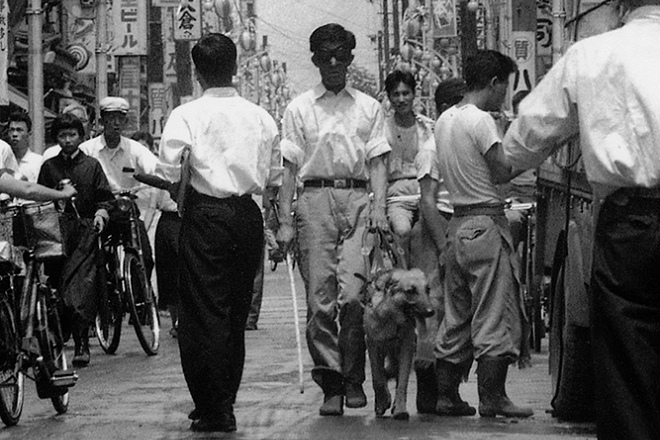 為了摸索導盲犬的訓練法，鹽屋賢一戴眼罩走在街上。 取自眼伴後援會