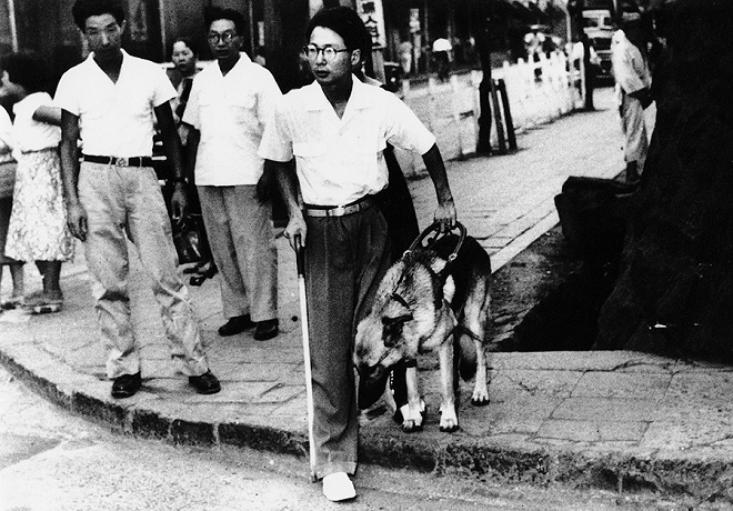 鹽屋賢一（左）在街上指導河相洌與強皮做步行訓練。 取自眼伴後援會