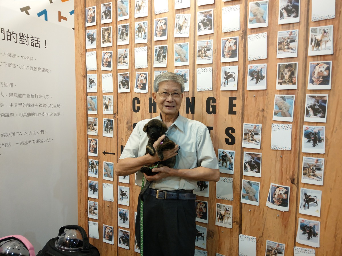 APA理事長李朝全與浪浪們的明信片牆合影,明信片上的每隻動物都是TATA過去1年送養出的浪浪。陳璽安/攝